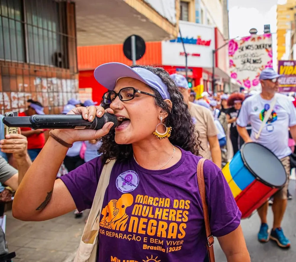 Carol Caldeira falando ao megafone durante ato de rua da Marcha das Mulheres Negras